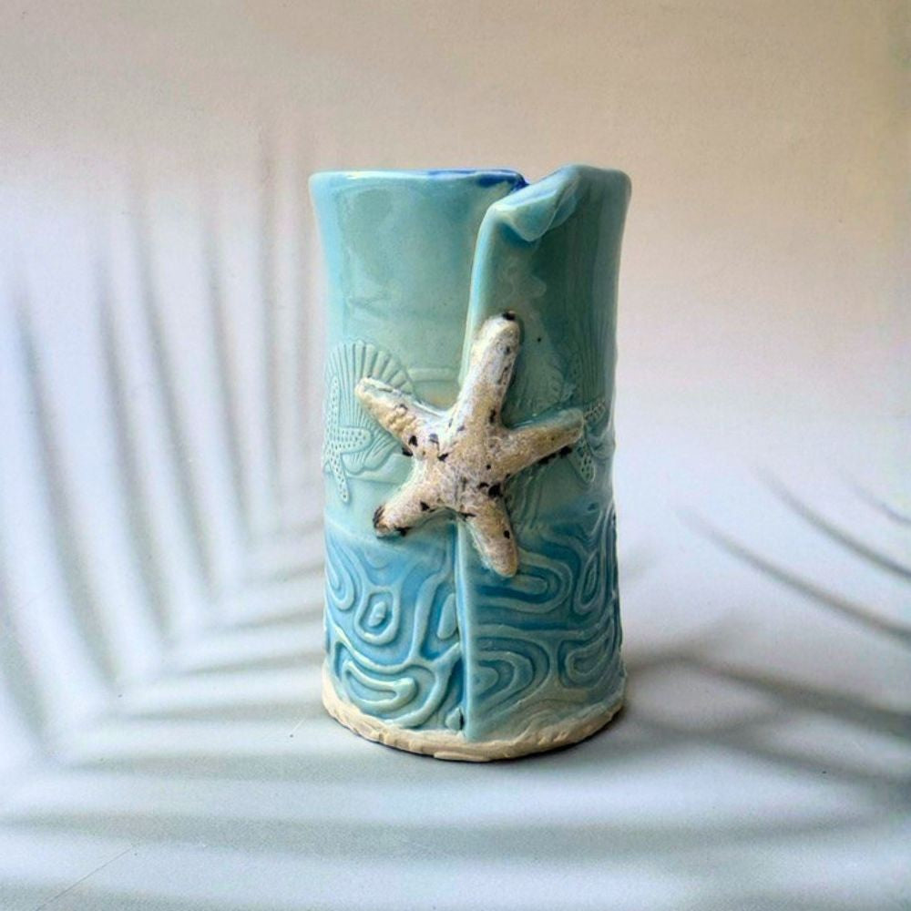 Turquoise ceramic bud vase with starfish design on a white background